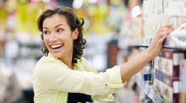 mujer en pasillo de supermercado sonriendo y revisando marcas de los anaqueles